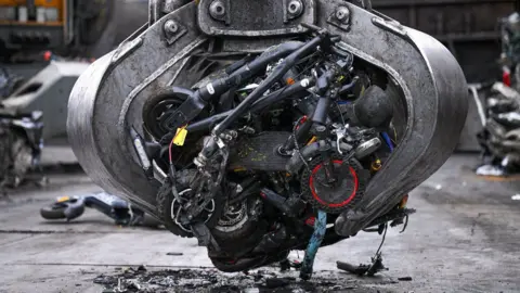 Dorset Police A large grabber of a scrapyard handling machine with several crushed scooters in its claws