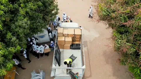 Waste to Wonder A birds-eye view of a truck with office cabinets on a sandy road surrounded by people.