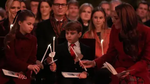 PA Catherine sits on the left of Louis and Charlotte. She is helping the children light tall white candles.