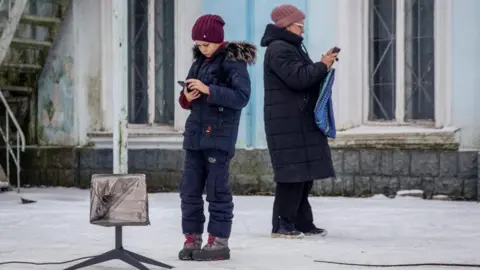 Reuters A boy and a woman stand in a snowy scene next to a Starlink terminal, using their electronic devices