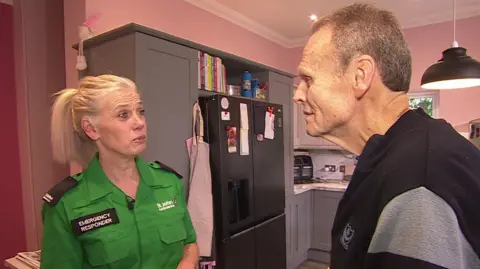 Sarah Taylor in her St John's Ambulance uniform stood in the Dewane family kitchen talking to Bob Dewane.