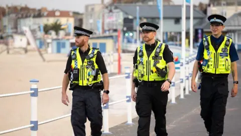 Dorset Police Three uniform officers on patrol along a beach front.