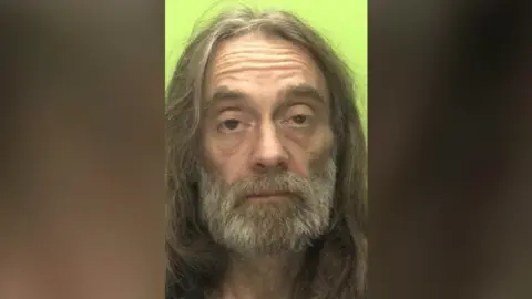 Nottinghamshire Police An image of Adrian Perry with long hair, a beard and brown eyes