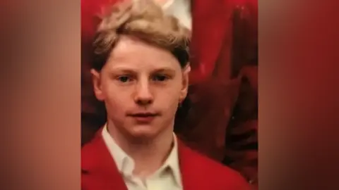 ANGUS BELL Angus Bell as a pupil at Loretto School in the 1990s wearing a red jacket over a white shirt.