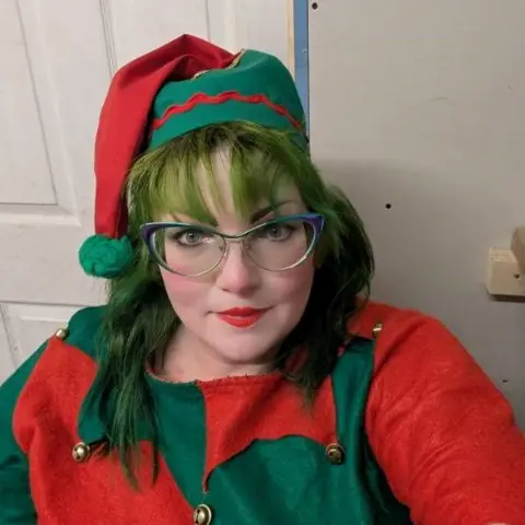 Lisa Miller made the image of Lisa Miller wearing her Elf dress. He has a purple colored glasses, green hair and a red-and-green boble hat. His top is also red and green.