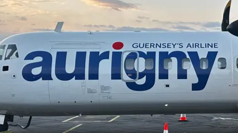 A picture of the side of a Aurigny plane. There is a white plan which reads in blue text - "Guernsey's Airline aurigny'