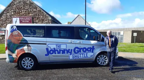 Valerie Boon A bus driver standing next to a small mini-bus with the words The Johnny Groat Shuttle on the side.