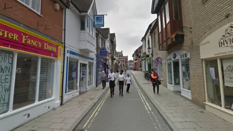 Google image of Sir Isaacs Walk in Colchester. There are shops on the side and people are walking on a narrow road.