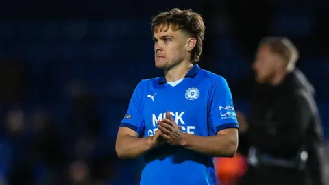 Getty Images Archie Collins wearing a Posh kit with his hands clasped together looking into the distance during a match. 