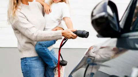 Getty Images Woman and daughter charging black electric car outside home