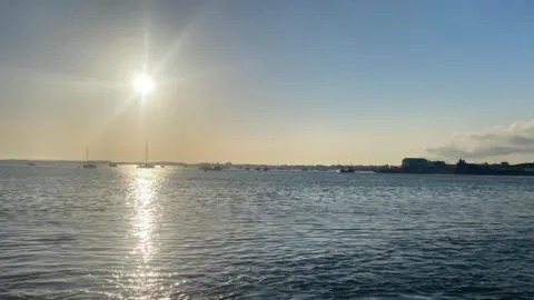 Coast Al The sun shines down on the sea leaving a dappled effect through the picture towards the horizon where boats pepper the surface