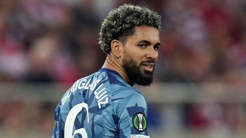 Douglas Luiz, wearing Aston Villa's blue away strip, looks over his right shoulder and stares to the right of the camera 