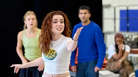 Birmingham Rep Charlotte Wallis rehearsing for the play wearing a white cropped tshirt. She's gesticulating. 
