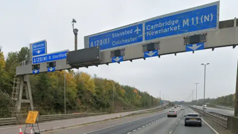 An overhead sign on a the M11 motorway showing lanes for A120 Stansted and Colchester and M11 for Cambridge and Newmarket