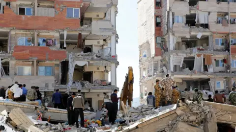 EPA Iranian people and soldiers stand around damaged buildings in the city of Sarpol-e Zahab in Kermanshah Province, Iran on13 November 2017.