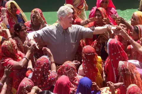 Getty Images US President Bill Clinton shakes hands with local villagers after touring Nayla Village 23 March 2000.