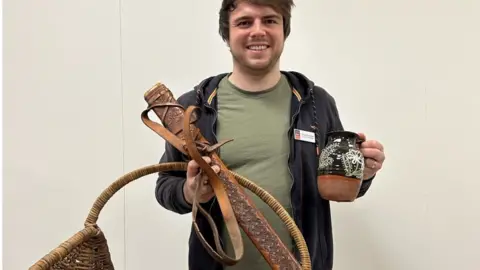 EACH EACH staff member holding some of the props including a black jug with white paintings on it and a sword sheath and wicker basket