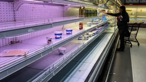 EPA A customer looks for dairy products left in a shelf in a supermarket in Caracas, Venezuela on 27 August 2018