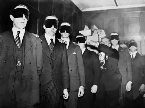 Gamma-Keystone via Getty Images A black and white photo shows a group of men being led wearing blindfolds through a room during an initiation ceremony at a Freemasonry Lodge in 1933.