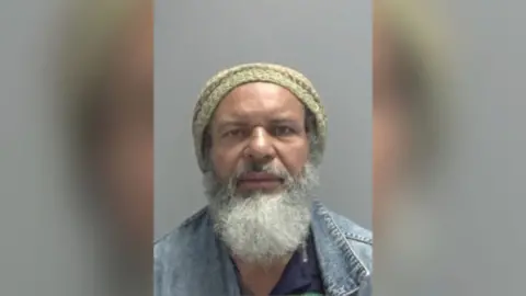 Norfolk Constabulary A police custody photo of Jose Da Silva Junior wearing a knitted hat. He has a grey beard and is wearing a denim jacket and navy T-shirt.