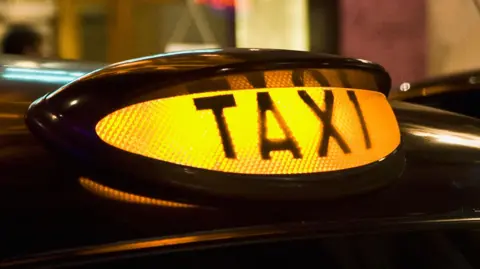 An orange illuminated 'taxi' sign on top of a car. 