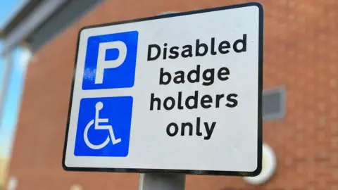 A white street sign with a parking symbol and a disability symbol. The text says 'Disabled badge holders only.' 