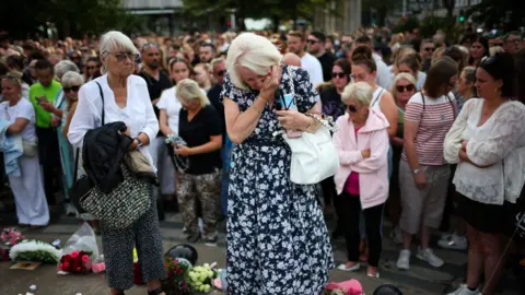 Reuters A woman wipes tears from her eyes as she looks at flowers that have been left for the victims of the Southport stabbing