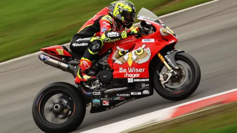 Getty Images Shane Byrne on a motorcycle on a track. The motorbike is red, with the crest of a bird's face on the side - either an owl or an eagle.