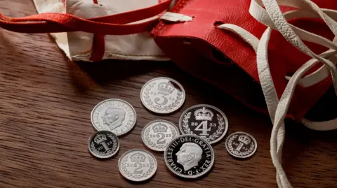Royal Mint Various coins with the head of King Charles III alongside the red Maundy purse.