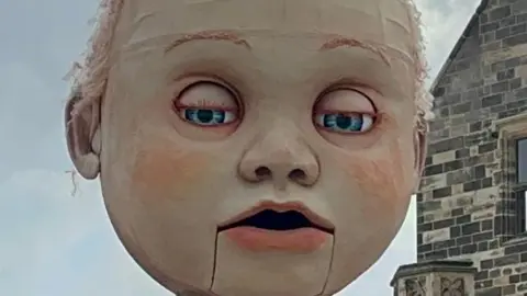 A close-up of the giant puppet's face, with its eyes half closed.