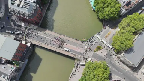 Avon and Somerset Police A drone shot above a bridge over a river in Bristol with people scattered on both sides. While all people look tiny, a number of police in high-viz can be spotted.