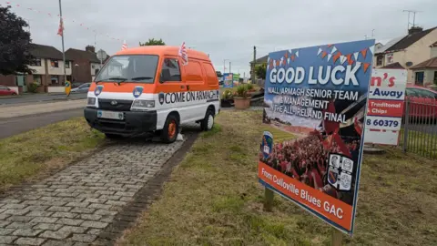 Orange and white delivery van next to a sign that says "GOOD LUCK"