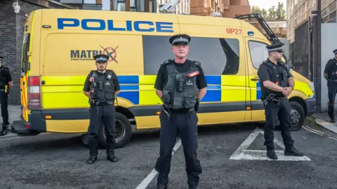 Merseyside Police officers guard LIverpool Magistrates Court standing in front of a yellow personnel carrier.