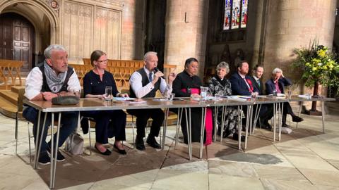 Eight people sat at a table in Gloucester Cathedral, including the dean of Gloucester