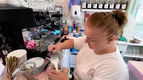 Martin Giles/BBC Tina Smart making coffee and pouring milk into a cup in cafe