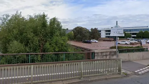 Google A landscape picture of a Bridge Street car park in Staines, showing half a dozen cars parked, with railings and the road in the foreground.