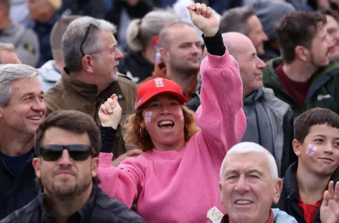 A woman in a pink jumper with the St George cross painted on her cheeks celebrates an England boundary against Australia in the one-day international in Bristol