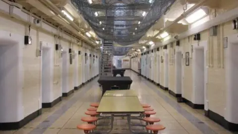 HMP Leeds interior, with tables and stools in the foreground, and a staircase in the background. Rows of cells are on either side.