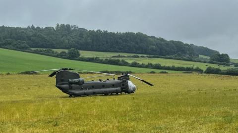 A Chinook helicopter in a field. The front section of the fuselage is wrapped in a silver cover