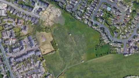 A satellite image of a field, surrounded by residential streets and houses.