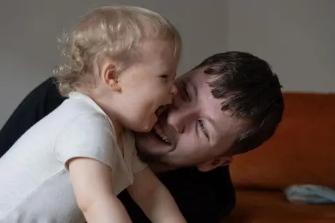 NEYDL Callum Fay has his face close to his young son Archie's face and is smiling while Archie laughs.