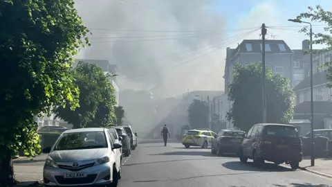 Police tape with smoky skyline beyond residential street with parked cars