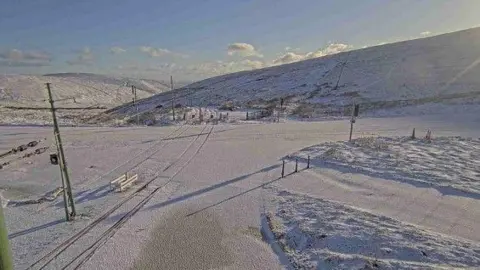 DOI Snow covering the Mountain Road at the electric railway crossing point, with Laxey Valley in the  background.