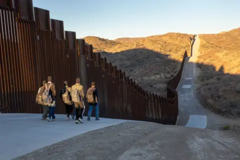 Getty Images Immigrants from India walk next to the Trump-built U.S.-Mexico border fence after crossing into Arizona on January 19, 2025 near Sasabe, Arizona. 