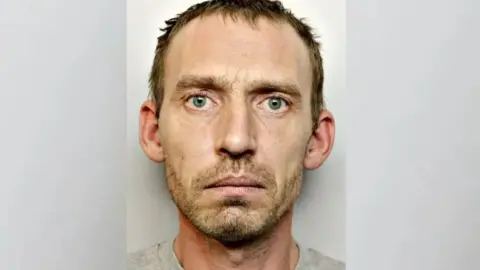 Avon and Somerset Police A police mugshot of a man with short dark hair and stubbly beard. 