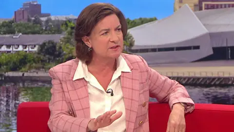 Eluned Morgan being interviewed on the bright red BBC Breakfast sofa, with images of Salford Quays on the screen behind.