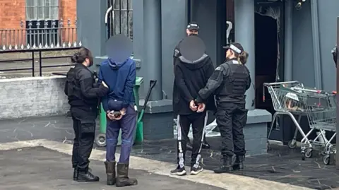 Officers lead two handcuffed men into the building 