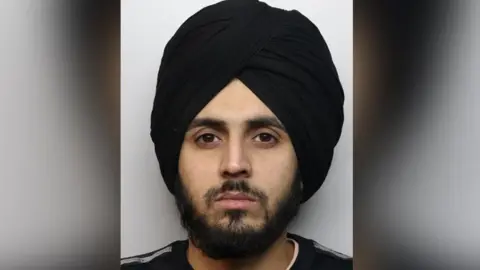 Aaron Kumar with a beard and a black turban looks into the camera. 