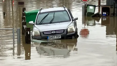 Simon Jones/BBC A silver KIA jeep left abandoned in a flooded area in Yalding, Kent, which is the subject of a flood warning by the Environment Agency. The silver jeep is part submerged in flood water.