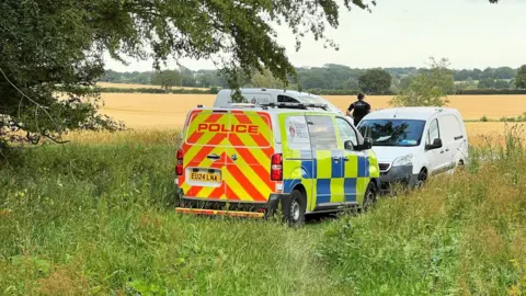 Stuart Woodward / BBC Three police vans parked on a field, with an officer looking away into the field.